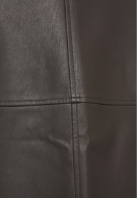 Material de cuero marrón oscuro con una textura suave, que presenta costuras visibles y un ligero brillo, destacando las costuras de los paneles.
