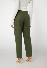 Pantaloni cargo verdi oliva con una vestibilità comoda, dotati di tasche laterali e dettagli cuciti. Abbinati a sandali beige con tacco alto.