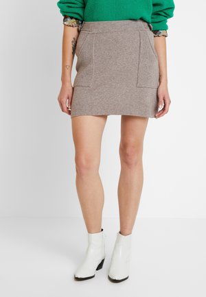 Mini-jupe grise en tricot avec des poches avant côtelées, une taille plate et un ourlet droit, associée à des bottines blanches. 