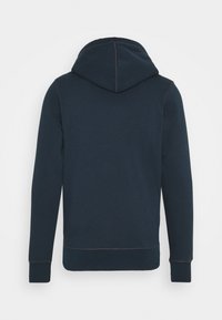 Felpa blu navy con maniche lunghe e cuciture marroni ben visibili, mostrata di spalle su uno sfondo bianco uniforme.