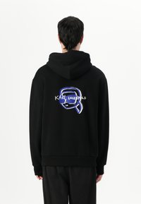 Felpa nera con cappuccio regolabile, caratterizzata da una stampa grafica blu e bianca sul retro con il testo "KARL LAGERFELD." Tessuto morbido.