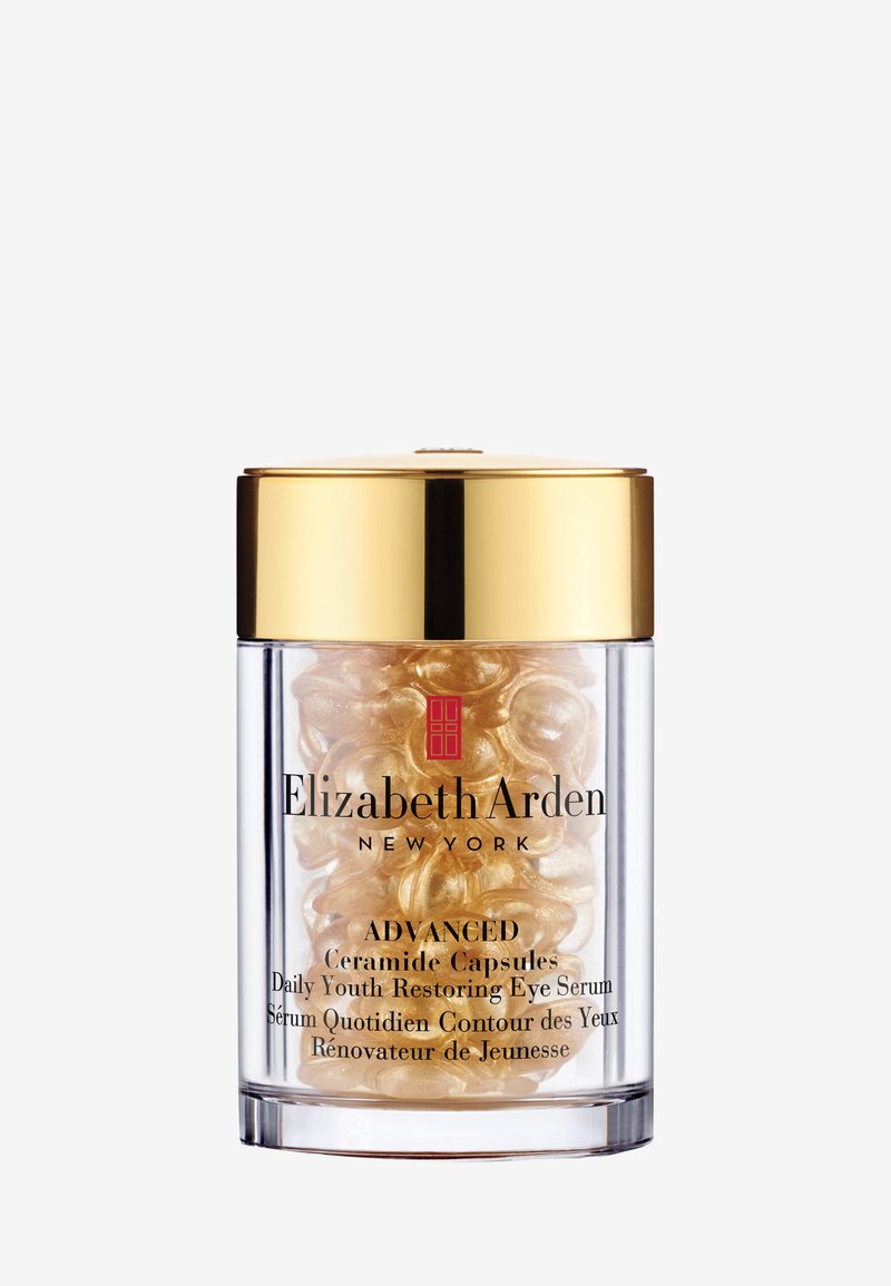 Conteneur cylindrique transparent avec un couvercle doré, rempli de capsules dorées, étiqueté "Advanced Ceramide Capsules Daily Youth Restoring Eye Serum."