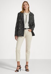 Zwart-wit tweed blazer met een dubbelzijdig ontwerp, gecombineerd met een gestreept shirt, crème broek en zwarte leren sandalen met hak.