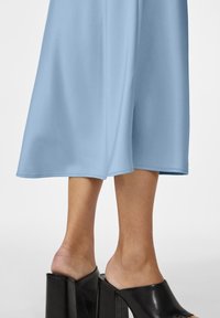 Vaaleansininen midimekko, jossa on sileä pinta, leveä helma ja laskeutuva siluetti, yhdistetty kiiltäviin mustiin platform-sandaaleihin.