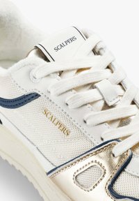 Zapatillas Scalpers en blanco y dorado con detalles de malla y cuero, cordones blancos y acentos en azul marino, mostrando las secciones lateral y frontal.