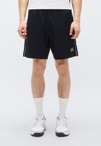 Námornícke športové šortky s elastickým pásom, bočnými pruhmi a logom EA v bielej farbe. Nosia sa s bielymi podkolienkami a teniskami.