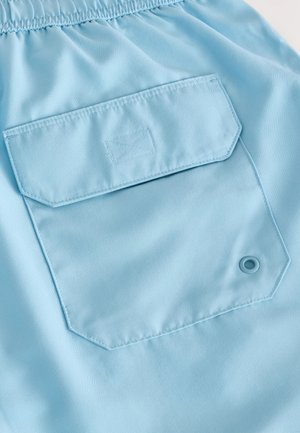 Lichtblauwe stof met een gladde textuur, voorzien van een rechthoekig zakje en een ronde ringenoog. Comfortabele taille met elastiek.