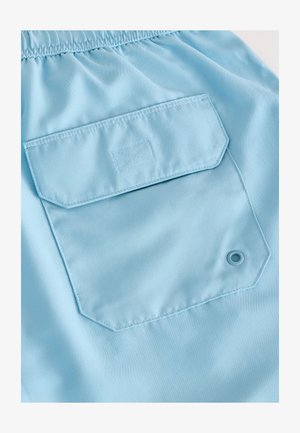 Lichtblauwe stof met een gladde textuur, voorzien van een rechthoekig zakje en een ronde ringenoog. Comfortabele taille met elastiek.