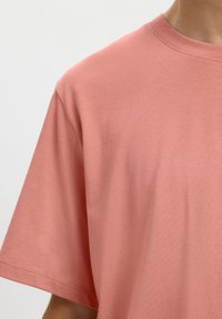 Βαμβακερό t-shirt σε απαλό κοραλλί με χαλαρή εφαρμογή, κοντά μανίκια και στρογγυλή λαιμόκοψη, με ομαλή υφή και ελάχιστες ραφές.