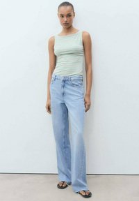 Striped sleeveless top in white, green, and pink; light blue jeans with a relaxed fit and high waist; black sandals with decorative hardware.