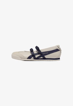 Chaussure plate beige avec des brides décoratives bleu marine et des double boucles, présentant une finition en cuir lisse, un bout arrondi et une semelle texturée.