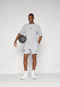 Gray athletic outfit featuring a loose t-shirt with a Lakers logo and matching shorts, paired with white sneakers and holding a basketball.