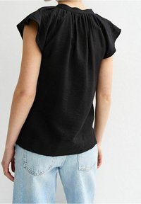 Haut noir à manches courtes avec un décolleté froncé, tissu texturé et coupe décontractée, associé à un jean taille haute bleu clair.