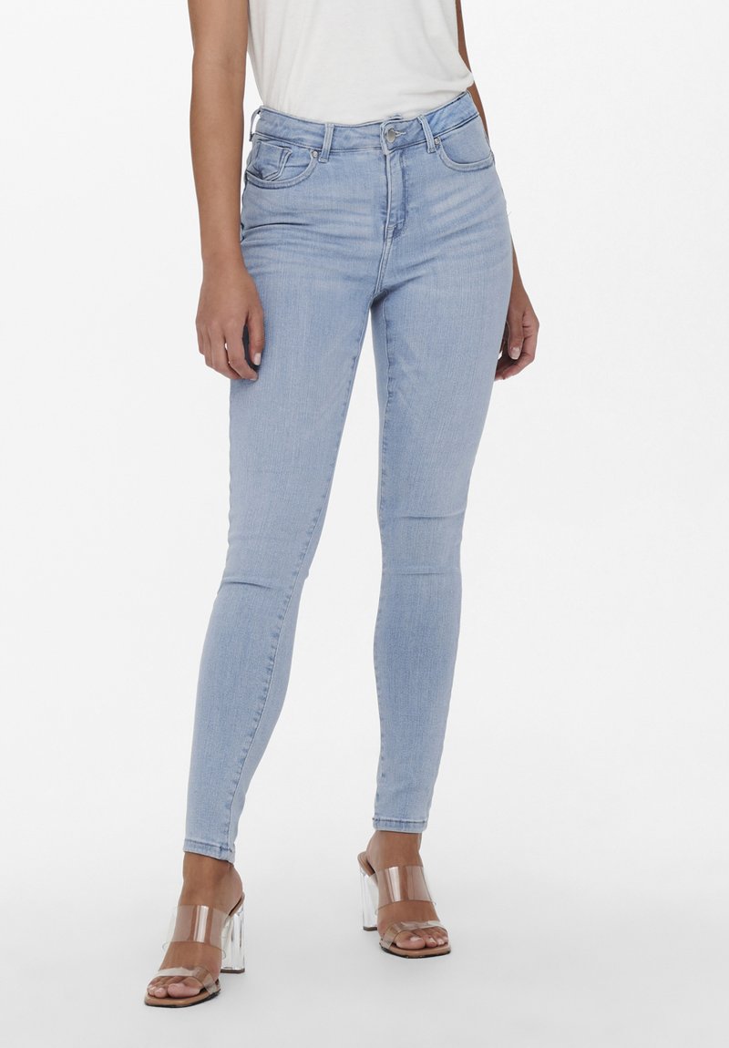 Lyseblå skinny jeans med høy midje, fem lommer og subtile sømdetaljer, kombinert med gjennomsiktige hælsandaler.