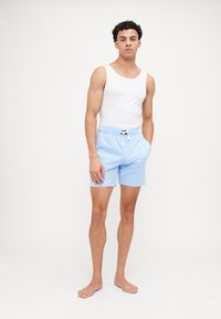 Calções de banho azul claro com cintura elástica, fecho por cordão e bolsos laterais; combinados com uma blusa branca sem mangas.