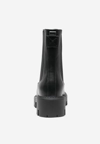 Botín negro hasta el tobillo con un acabado de cuero texturizado, cremallera trasera y una suela gruesa con surcos para mayor tracción. Elementos de diseño verticales acentúan su forma.