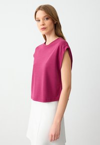 T-shirt cropped a maniche corte di un vivace magenta, con colletto rotondo e texture morbida e liscia. Design minimalista senza fantasie visibili.