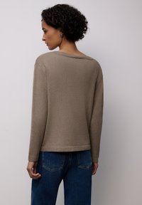 Béžový pletený svetr se širokým výst�řihem, žebrovanými manžetami a lemem. Nositelný přes tmavě modré džíny, zobrazený zezadu. Texturovaná látka.