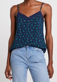 Mörkblå ärmlös topp med grönt bladmönster, med V-ringning, knappdetaljering och tunna axelband. Texturerad tyg, avslappnad passform.