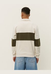 Beige sweatshirt met een donkergroene horizontale streep, ribgebreide manchetten en kraag. Ontspannen pasvorm met een gladde textuur. Achteraanzicht weergegeven.