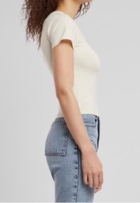 Ljusbeige, figursydd t-shirt med korta ärmar, hög halsringning och mjukt bomullsmaterial, i kombination med högmidjade blå denimjeans.