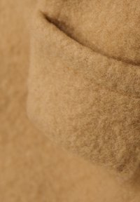 Tissu en laine doux de couleur brun clair avec une texture subtile, présentant un détail de bord replié. Vue de près mettant en avant la chaleur du matériau.