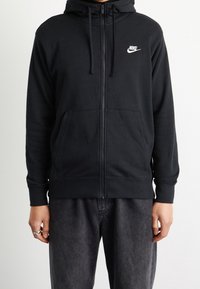 Svart zip-up hoodie i bomullsblandning. Har en framficka, dragsko i huvan och en liten vit Nike-logotyp på bröstet.