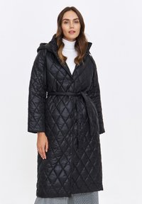 Czarny pikowany długi płaszcz z kapturem, paskiem i wzorem rombów. Posiada zapięcie na guziki oraz miękką, błyszczącą teksturę.