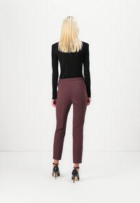 Top preto com relevo de mangas compridas combinado com calças burgundy ajustadas. Sapatos pretos de salto alto com tiras no tornozelo. Textura suave e design ajustado.