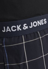 Mannen zwarte geruite boxers met een zachte marineblauwe tailleband waarop "JACK & JONES" in witte letters staat, gemaakt van katoen en voorzien van een geruit patroon.
