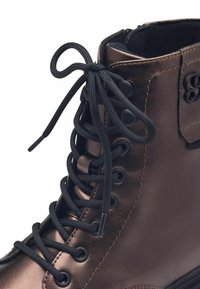 Bota alta de imitación de cuero marrón con diseño de cordones negros, featuring ojetes redondos y un collar acolchado para mayor comodidad.