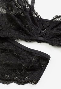 Bralette in pizzo nero e culotte abbinati con motivo floreale, tessuto testurizzato, spalline regolabili e vita elastica.