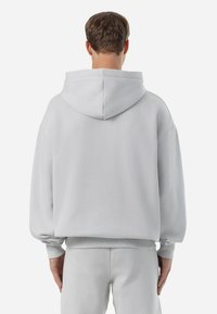 Sweatshirt cinza claro feito de algodão, apresentando um corte largo, capuz grande e punhos e bainha canelados. Textura lisa, com detalhes de costura mínimos.