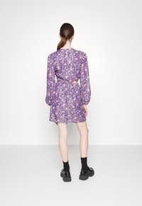 Fialové květinové šaty s nafouknutými rukávy, výstřihem na zádech a elastickým pasem. Kombinované s černými masivními botami a tmavými ponožkami.