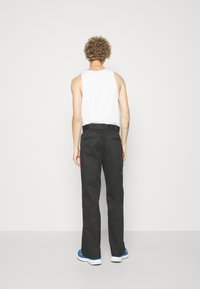Black trousers with a straight fit, belt loops, and back pockets. Worn with a white tank top and blue sneakers. Smooth texture, minimal design.
