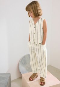 Ensemble deux pièces comprenant un haut sans manches à col en V avec des rayures verticales et un pantalon léger et ample assorti, le tout en crème et noir.