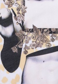 Närbild av överkroppen med höjd arm, svartvitt topp och detaljerade blommönster och löv som överlagras på arm- och bröstområden.