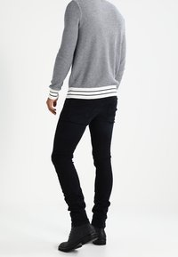 Szary sweter dzianinowy z białymi i granatowymi paskami na mankietach, zestawiony z czarnymi obcisłymi jeansami i czarnymi botkami za kostkę. Gładka faktura, dopasowany krój.