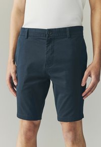 Marineblå bomuldsshorts med flad front, enkelt knaplukning og sidelommer. Glat tekstur og knælang længde.