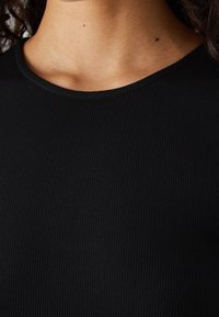 Černá žebrovaná látka s kulatým výstřihem. Detailní pohled zdůrazňující texturu a hladkost. Žádné další vzory nebo akcenty nejsou viditelné.