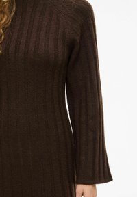 Pull en maille côtelée marron à manches longues, présentant une texture douce et un design ajusté. Le tissu affiche un éclat subtil et une profondeur.