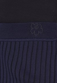 Marinblå ribbad väv med en slät midja. En subtil präglad blomdetalj finns på midjan för att ge extra textur.