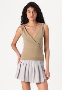 Beige omslagstopp med dyp V-hals, sammen med en lys grå plisseh skirt laget av mykt stoff, med strukturerte plisser.