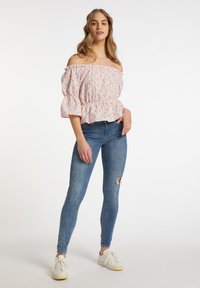 Růžová květinová blůza s odkrytými rameny, s nafouknutými rukávy a volánkovým lemem, kombinovaná s vytahanými modrými skinny džíny a bílými teniskami.