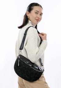 Borsa nera a forma di mezzaluna, realizzata in materiale testurizzato. Presenta una finitura lucida, una chiusura con zip e una tracolla regolabile.