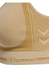 Beige sportbh med en texturerad yta i ribbat tyg och ett brett band. Inkluderar en logotyp och detaljer i ett chevronmönster.