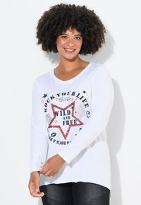 Valkoinen pitkähiha Shirt, jossa on graafinen printti, jossa on punainen tähti ja teksti "VILLI JA VAPAA" mustilla, hopeisilla ja vaaleanpunaisilla yksityiskohdilla.