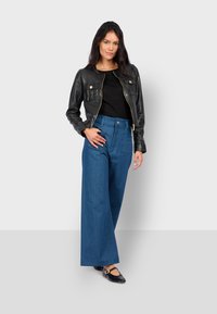 Černá kožená bomber bunda se zipem, zlatými detaily, dlouhé modré široké džíny a černé boty s páskem. Jednoduchý, strukturovaný silueta.