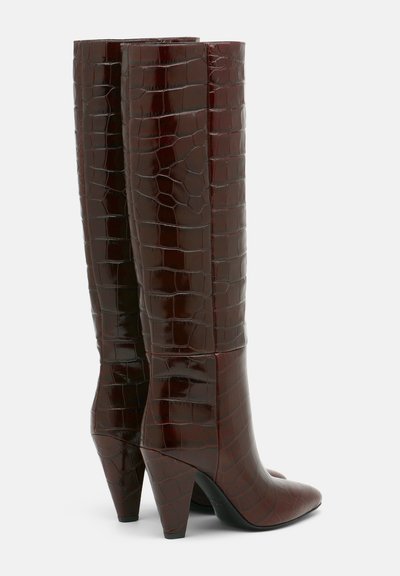 Botas de rodilla brillantes en burdeos con textura de cocodrilo. Cuentan con punteras afiladas y tacones en bloque para mayor estabilidad.