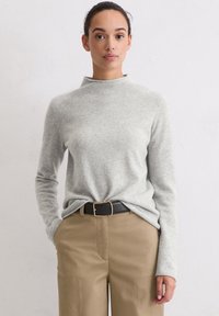 Lichtgrijze trui met een hoge hals en lange mouwen, gemaakt van zachte stof. Gecombineerd met beige broek en een zwarte riem met een gouden gesp.